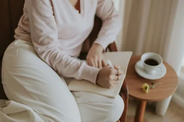 person sitting near a window writing in their diary